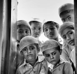 pexels-photo-14325725-14325725 A group of children in traditional attire gazing through a window with solemn expressions.